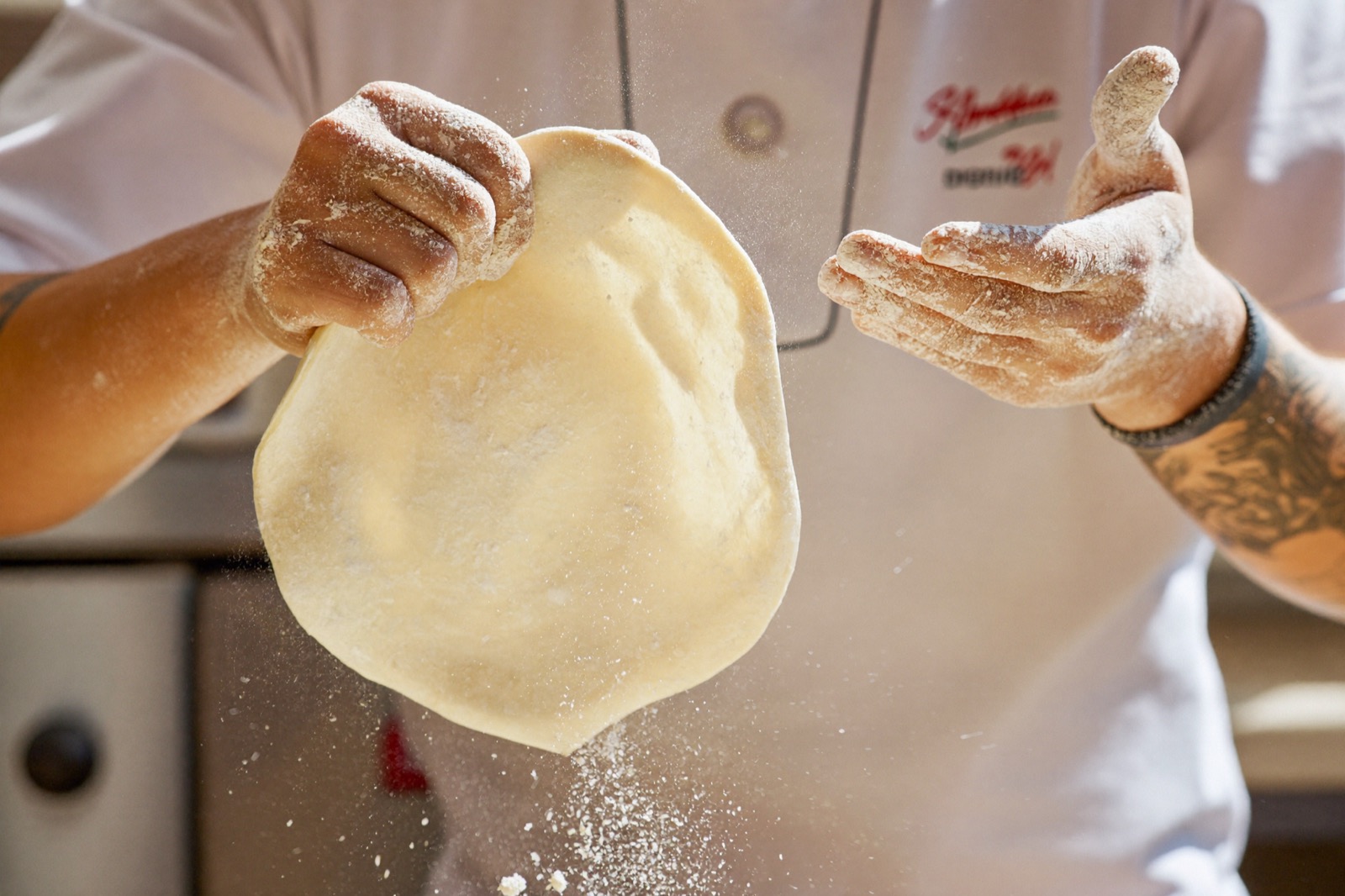 Mains d'un pizzaiolo étirant la pâte dans un nuage de farine